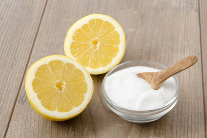 un limón cortado junto a un bol de ácido anhidro en polvo sobre una mesa de madera
